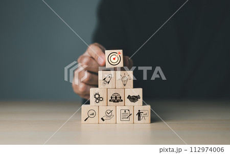 Business goals and target success concepts. Businessman places wooden blocks with business icons. business growth, Achievement company, corporate startup, investment goal, Planning ideas and strategy, 112974006
