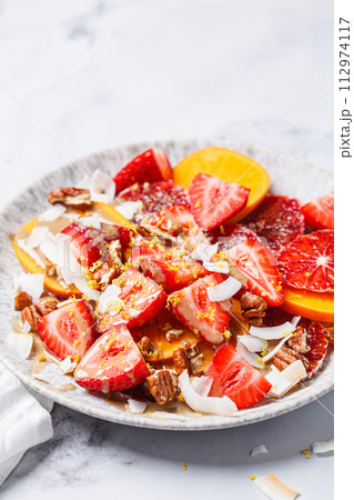 Fruit salad with persimmon, orange, strawberries, coconut chips and lemon zest. 112974117