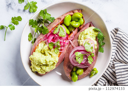 Baked sweet potato halves with guacamole, edamame beans, pickled red onion and cilantro. 112974133