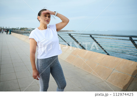 Portrait of a female athletic runner looking into the distance while resting after morning jog on the Atlantic promenade Portrait of a female athletic runner looking into the distance while resting after morning jog on the Atlantic promenade 112974425