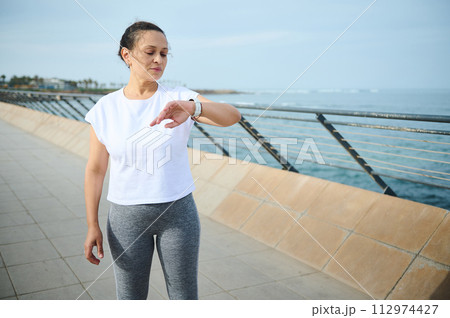 Exhausted woman runner check heart beat of fitness app on her modern smart wristwatch, after outdoor workout in the city 112974427