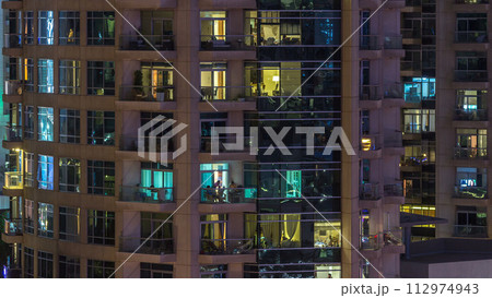 Windows of the multi-storey building of glass and steel lighting inside and moving people within timelapse 112974943