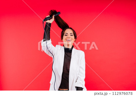 Happy young woman with beautiful hair holding curling iron on grey and red background 112976078