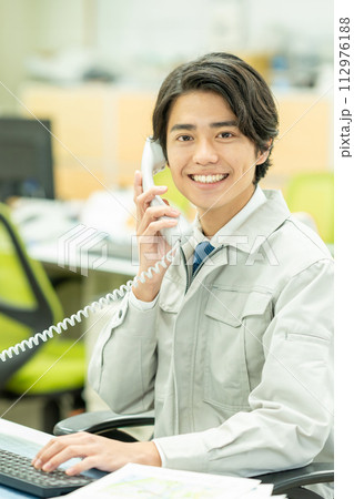 オフィスで電話をする作業服の若い男性 オフィスで電話をする作業服の若い男性 112976188