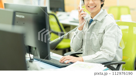 オフィスで電話をする作業服の若い男性 112976190