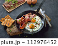 Crunchy fried eggs with Italian pancetta bacon served  in an old iron frying pan on rustic weathered wood 112976452