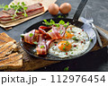Crunchy fried eggs with Italian pancetta bacon served  in an old iron frying pan on rustic weathered wood 112976454