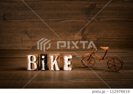 BIKE. Text from alphabet blocks and rusty miniature bicycle on wood texture background BIKE. Text from alphabet blocks and rusty miniature bicycle on wood texture background 112976619