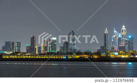 Modern Dubai city skyline timelapse at night with illuminated skyscrapers over water surface Modern Dubai city skyline timelapse at night with illuminated skyscrapers over water surface 112976698
