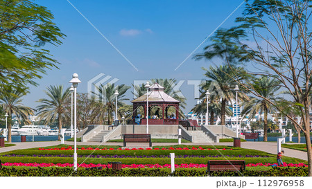Alcove with green lawn, flowers and trees at Dubai Creek park timelapse. Dubai, United Arab Emirates 112976958