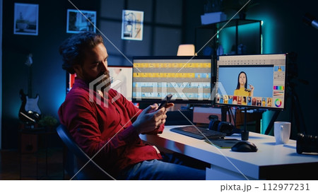 Photographer taking break from using photo editing software on PC display, texting friends to relax. Freelancer stops using photographs retouching program to spend time on mobile phone Photographer taking break from using photo editing software on PC display, texting friends to relax. Freelancer stops using photographs retouching program to spend time on mobile phone 112977231