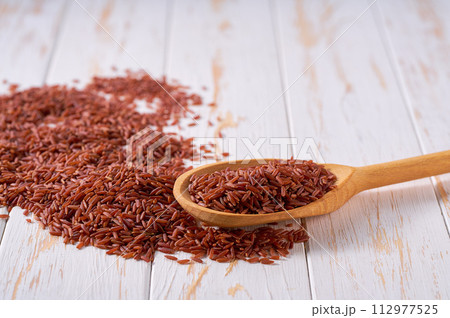Raw red rice crumble from in a wooden spoon on a white wooden table. 112977525