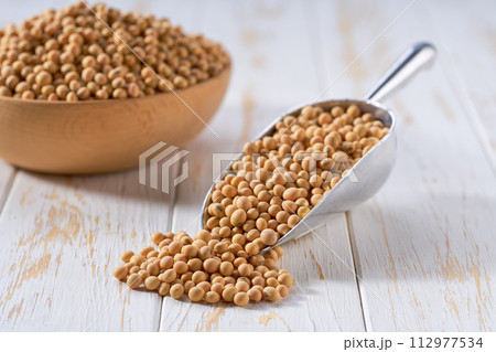 Raw soybeans in a metal scoop on a white wooden table. Raw soybeans in a metal scoop on a white wooden table. 112977534