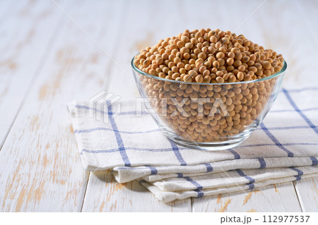 Raw soybeans in a glass plate on a white wooden table. 112977537