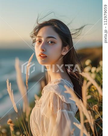 夕日を浴びて海の見える丘に立つ女性モデル 112979059