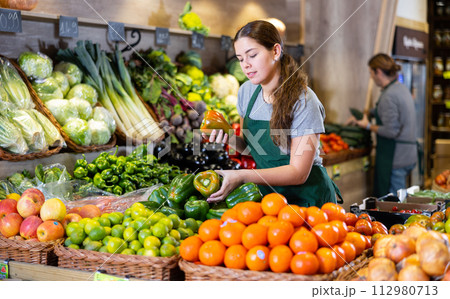Female seller holding green peppers standing in fruit and vegetable section of supermarket 112980713