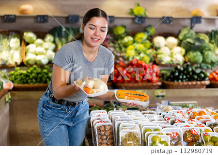 Woman picking out packaged papaya and carrots to buy in fruit and vegetables aisle of supermarket Woman picking out packaged papaya and carrots to buy in fruit and vegetables aisle of supermarket 112980719