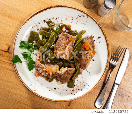 There is plate with braised french green bean and carrot and beef tenderloin stew on wooden table. 112980725