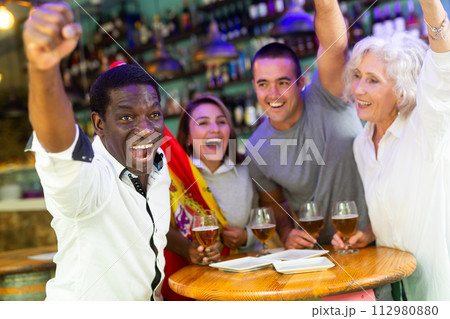 Cheerful international sport football fans waving Spanish flag and drinking beer in the sport bar 112980880