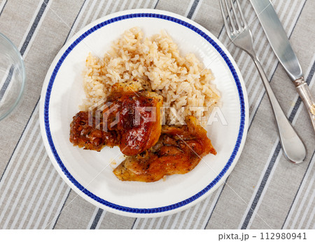 Baked chicken thighs served with rice on plate 112980941