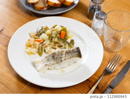 There is plate with fried cod fillet and braised french green bean on wooden table. 112980943