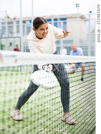 Woman serving ball while playing padel in court during training Woman serving ball while playing padel in court during training 112981029
