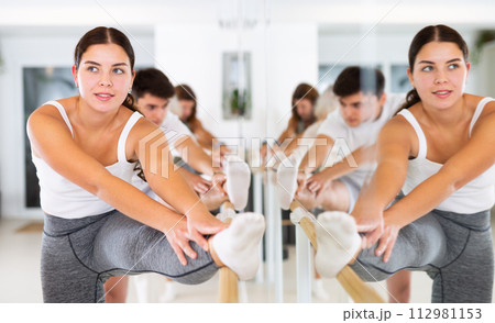 Young concentrated woman rehearsing ballet dance with other dancers in training room. Young concentrated woman rehearsing ballet dance with other dancers in training room. 112981153