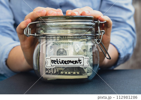 Unrecognizable woman holding Glass jar full of American currency dollars cash banknote with text RETIREMENT. Preparation saving money. Moderate consumption and economy 112981286