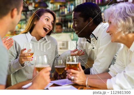 Mixed age range people celebrating holiday together in pub, toasting with drinks. Selective focus on people 112981300