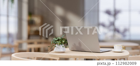 A back view image of a laptop computer on a wooden table in a modern cozy neutral coffee shop. 112982009