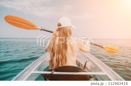 Woman in kayak back view. Happy young woman with long hair floating in transparent kayak on the crystal clear sea. Summer holiday vacation and cheerful female people relaxing having fun on the boat 112983418