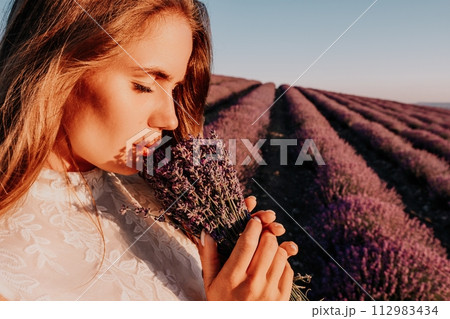 Woman lavender field. Happy carefree woman in a white dress walking in a lavender field and smelling a lavender bouquet on sunset. Ideal for warm and inspirational concepts in wanderlust and travel. Woman lavender field. Happy carefree woman in a white dress walking in a lavender field and smelling a lavender bouquet on sunset. Ideal for warm and inspirational concepts in wanderlust and travel. 112983434