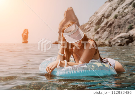 Woman summer sea. Happy woman swimming with inflatable donut on the beach in summer sunny day, surrounded by volcanic mountains. Summer vacation concept. Woman summer sea. Happy woman swimming with inflatable donut on the beach in summer sunny day, surrounded by volcanic mountains. Summer vacation concept. 112983486
