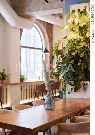 Vertical no people shot of part of modern restaurant interior with flowers in glass vase on wooden table, copy space 112984559