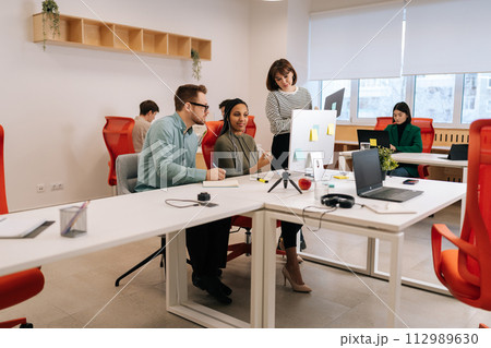 Remote view of diverse colleagues working together discussing computer project teamwork. Multiethnic business people of startup team coworkers cooperating sitting at work in modern corporate office. 112989630