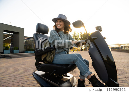 Woman tourist riding a four wheel mobility electric scooter on a city street 112990361