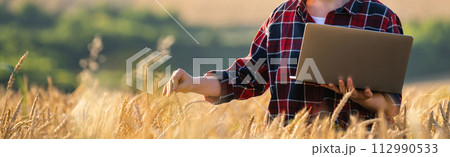 Female farmer working with laptop on wheat field. Smart farming and digital agriculture. 112990533