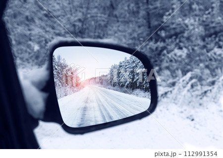 The winter road is reflected in the rear mirror of the car. Close-up 112991354