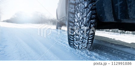 Car is on a snow covered winter road. Close up of winter tire 112991886