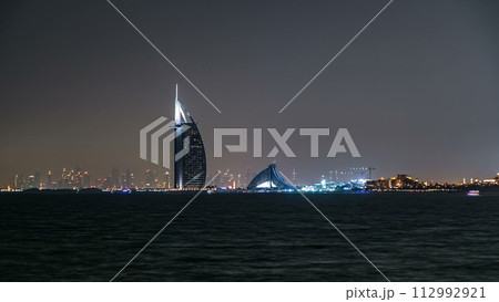 Skyline of Dubai at night timelapse with Burj al Arab in foreground in Dubai, United Arab Emirates Skyline of Dubai at night timelapse with Burj al Arab in foreground in Dubai, United Arab Emirates 112992921