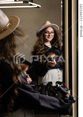 Female portrait of a hairdresser. A young barber girl blows her hair with air from the dryer. 112993293
