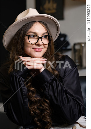 Portrait of a young girl in a hat and with long hair. A female student is sitting in the classroom during a break between pairs. Portrait of a young girl in a hat and with long hair. A female student is sitting in the classroom during a break between pairs. 112993296