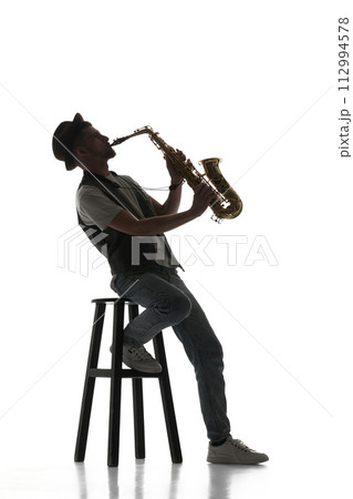 Talented young man making creative performance, playing saxophone isolate don white background. Black and white image. Talented young man making creative performance, playing saxophone isolate don white background. Black and white image. 112994578