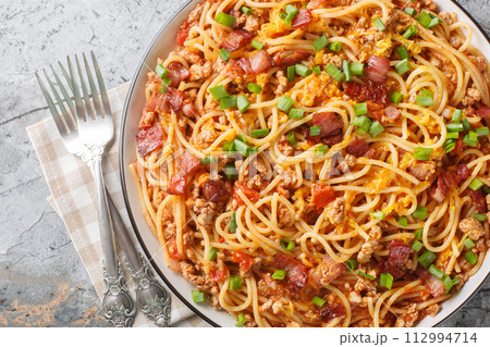 American spaghetti with bacon, minced meat, cheddar cheese and spicy tomato sauce close-up in a plate. Horizontal top view 112994714