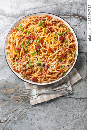 Western Cowboy Spaghetti with the addition of Ground beef, bacon, cheddar cheese, onion and hot sauce closeup on the plate. Vertical top view Western Cowboy Spaghetti with the addition of Ground beef, bacon, cheddar cheese, onion and hot sauce closeup on the plate. Vertical top view 112994715