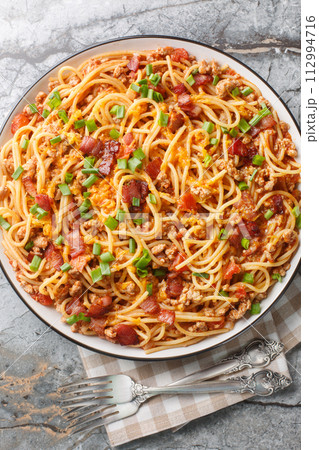 Cowboy Spaghetti with Ground beef, bacon, cheddar cheese, onion, pepper and tomatoes closeup on the plate. Vertical top view 112994716
