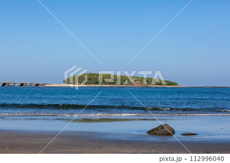 青空の下に隆起海床できた上に貝殻が蓄積しできた島に神様が祀られその周りには、鬼の洗濯岩や侵食さ波状岩 112996040