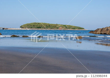 青空の下に隆起海床できた上に貝殻が蓄積しできた島に神様が祀られその周りには、鬼の洗濯岩や侵食さ波状岩 112996044