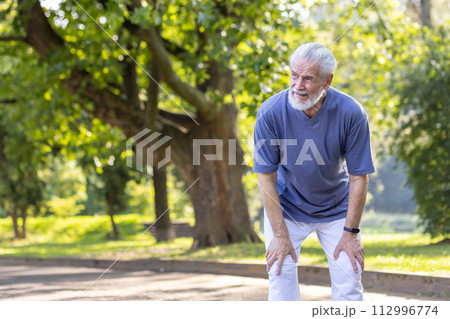 Tired senior gray-haired man is standing bent over in the park and resting after an active walk, run and workout. Tired senior gray-haired man is standing bent over in the park and resting after an active walk, run and workout. 112996774