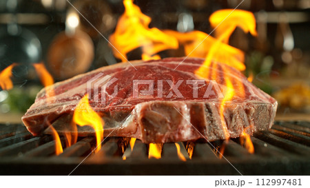 Close-up of tasty raw beef steak on cast-iron grate with fire flames Close-up of tasty raw beef steak on cast-iron grate with fire flames 112997481